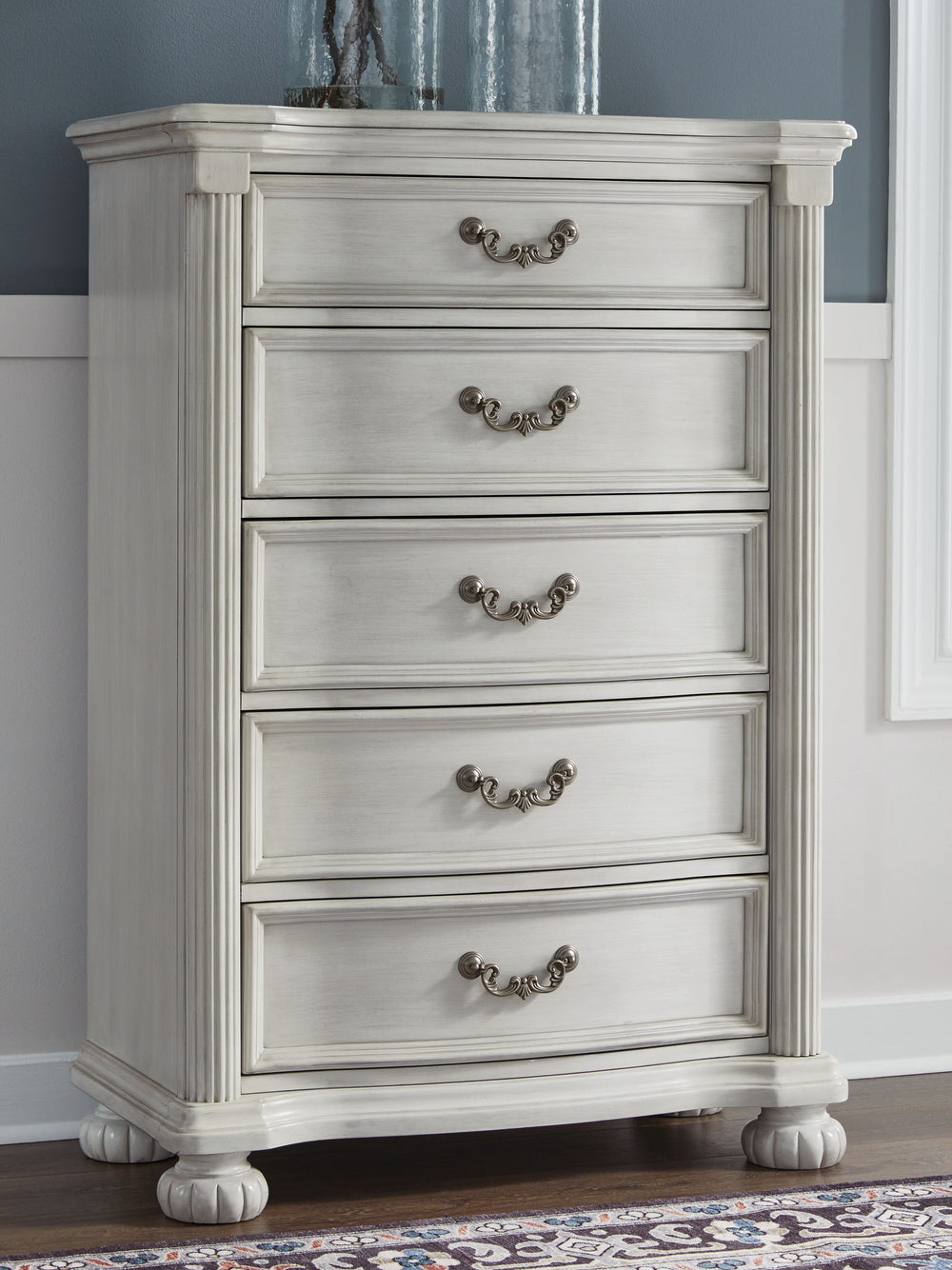 Transform your inner sanctum into a haven of timeless elegance and functionality. This traditionally styled chest of drawers is adorned in a classic antiqued white finish, highlighted by a serpentine-shaped front with thick decorative moulding. Its drawer